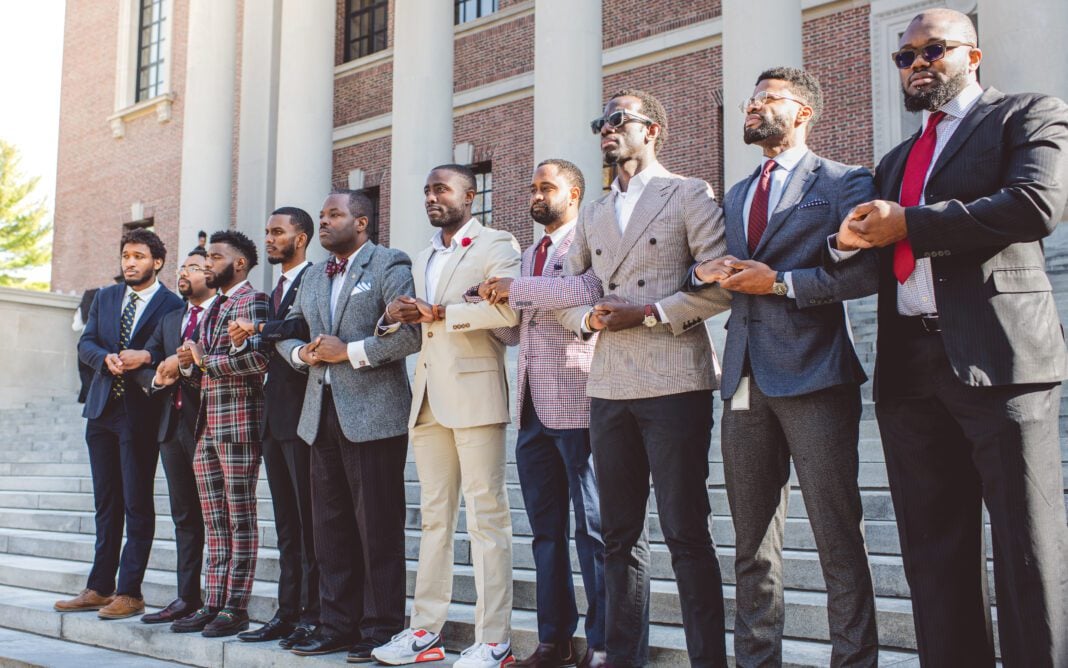 Black men enrolled at Harvard University with arms interlocked in front of Widener Library in Cambridge, Massachusetts. Individuals pictured from left to right: Nasir Stovall, Jordan Biggers, Taylon Lancaster, Ahmaad Edmund, Kevin Ross, Korde Innis, Kenneth Asher, Michael Bediako, Borniface Kabongo, Chika Okafor. (Photo/Corban Swain)