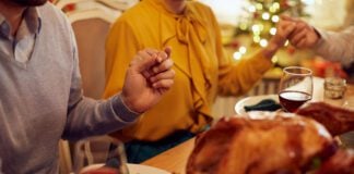 Close-up of family holding hands and praying before a meal on Christmas at dining table.