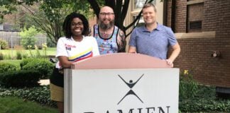 three people pose in front of damien center