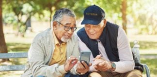 Elderly men, friends and phone in park, reading and army memory with thinking, relax and sunshine. Senior military veteran, smartphone and talk on bench, nostalgia and remember service in global war