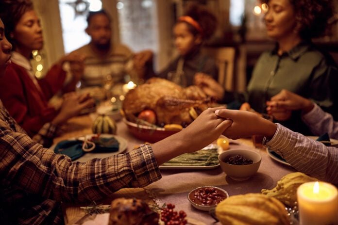 Close up of black brothers holding hands while praying with their family during dinner on Thanksgiving. Close of kids saying grace while having Thanksgiving dinner with their family at dining table. (Photo/Getty Images)